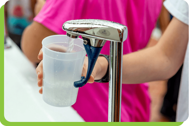 A person holding a cup of water at the drinking fountain.